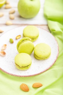 Green macarons or macaroons cakes with cup of coffee on a white wooden background and green linen