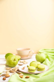 Green macarons or macaroons cakes with cup of coffee on a white and orange background and green