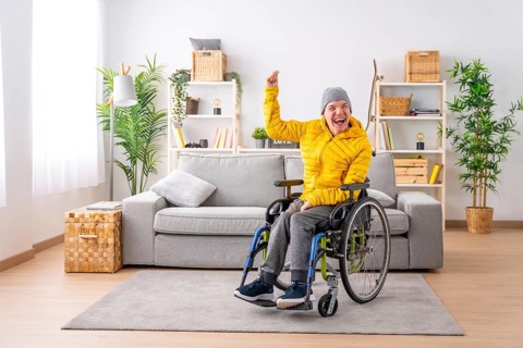 Portrait with copy space of a disabled man in wheelchair celebrating raising fist at home