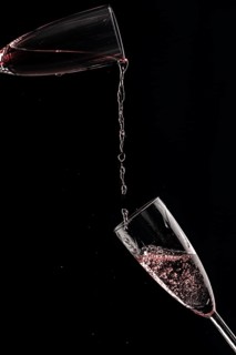 Rose champagne is poured from one champagne glass into another against a black background
