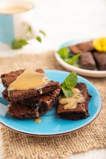 Chocolate brownie with caramel sauce with a cup of coffee on gray concrete background and linen