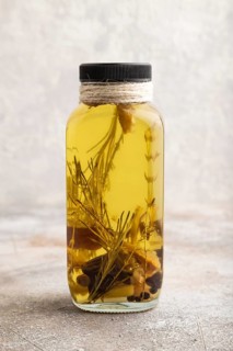Sunflower oil in a glass jar with various herbs and spices, lavender, sesame, rosemary on a brown