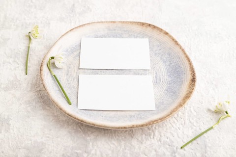 White paper invitation card, mockup with galanthus snowdrop flowers on ceramic plate and gray