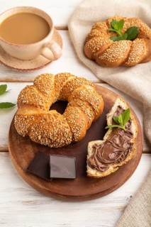 Homemade sweet bun with chocolate cream and cup of coffee on a white wooden background and linen