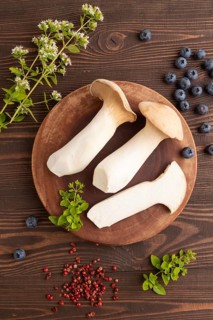 King Oyster mushrooms or Eringi (Pleurotus eryngii) on brown wooden background with blueberry,