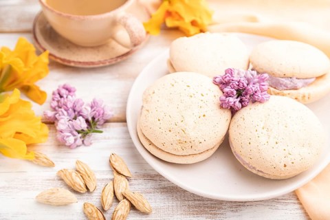 Meringues cakes with cup of coffee on a white wooden background and orange linen textile. Side