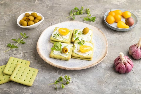 Green cracker sandwiches with cream cheese and cherry tomatoes on gray concrete background. side