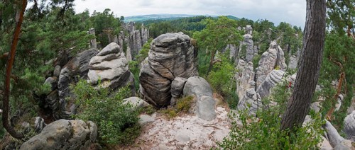 A panoramic view over bizarre rock structures surrounded by forest under a partly cloudy sky,