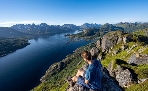 Mountaineer sitting on the summit of Dronningsvarden or Stortinden, behind mountains and fjord