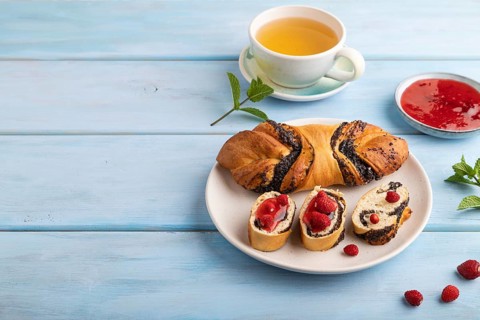 Homemade sweet bun with strawberry jam and cup of green tea on a blue wooden background. side view,