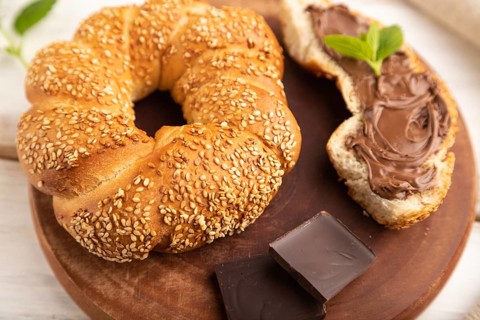 Homemade sweet bun with chocolate cream and cup of coffee on a white wooden background and linen