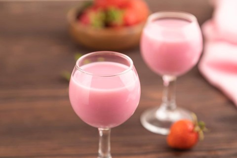 Sweet strawberry liqueur in glass on a brown wooden background and pink textile. side view, close