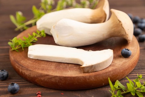 King Oyster mushrooms or Eringi (Pleurotus eryngii) on brown wooden background with blueberry,
