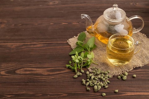 Green oolong tea with herbs in glass on brown wooden background and linen textile. Healthy drink