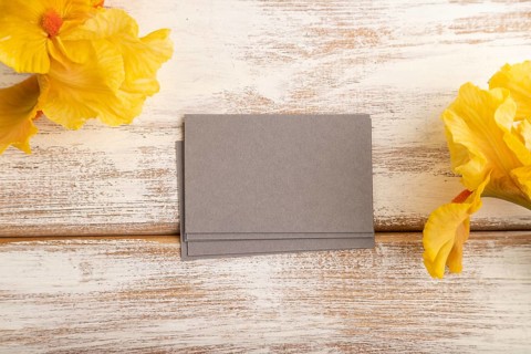 Gray business card with iris yellow flowers on white wooden background. top view, flat lay, copy