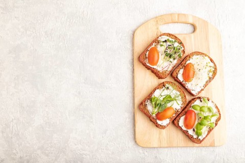 Red beet bread sandwiches with cream cheese, tomatoes and microgreen on gray concrete background.