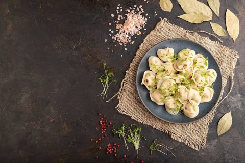 Dumplings with pepper, salt, herbs, microgreen on black concrete background and linen textile. Top