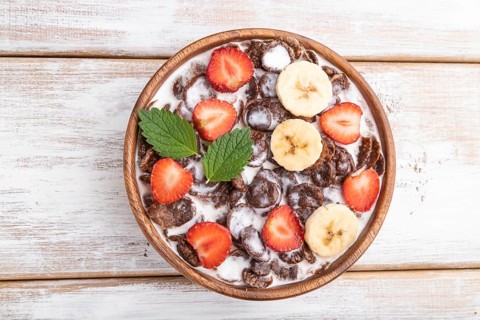 Chocolate cornflakes with milk and strawberry in wooden bowl on white wooden background. Top view,