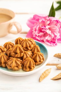 Homemade soft caramel fudge candies on blue plate and cup of coffee on gray concrete background,