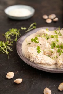 Stewed chicken fillets with coconut milk sauce and rucola microgreen on black concrete background