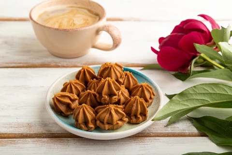Homemade soft caramel fudge candies on blue plate and cup of coffee on white wooden background,