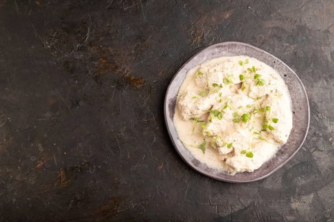 Stewed chicken fillets with coconut milk sauce and rucola microgreen on black concrete background.