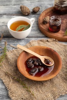 Pine cone jam with herbal tea on gray wooden background and linen textile. Side view, close up