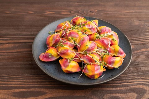 Rainbow colored dumplings with pepper, herbs, microgreen on brown wooden background. Side view,
