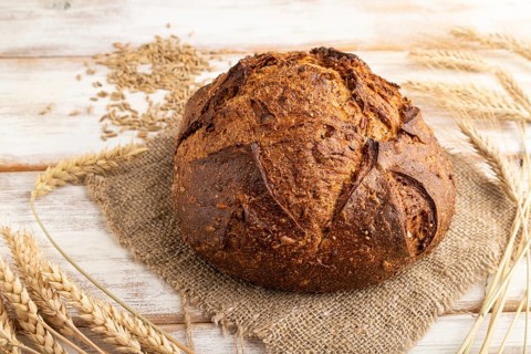 Fresh homemade golden grain bread with ears of wheat and rye on white wooden background and linen