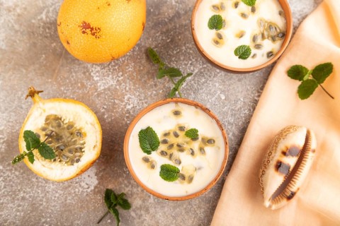 Yoghurt with granadilla and mint in clay bowl on brown concrete background and orange linen textile