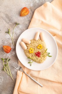 Funny mixed quinoa porridge, sweet corn, pomegranate seeds and small sausages in form of cat face
