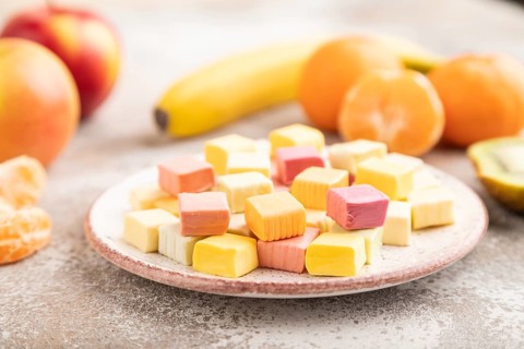 Various fruit jelly chewing candies on plate on brown concrete background. apple, banana,