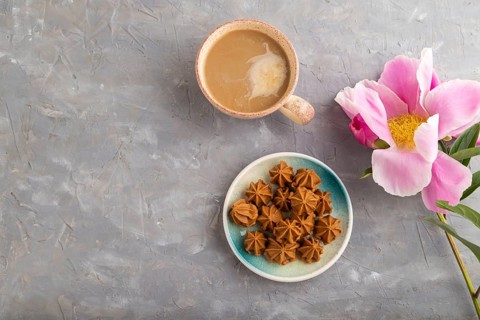 Homemade soft caramel fudge candies on blue plate and cup of coffee on gray concrete background,