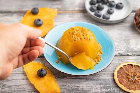 Mango and passion fruit jelly with blueberry with hand on gray wooden background. side view, close