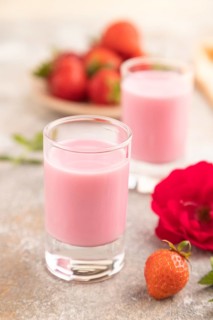 Sweet strawberry liqueur in glass on a gray concrete background and orange textile. side view,