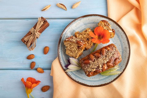 Caramel and almond cake with cup of coffee on blue wooden background and orange linen textile. top