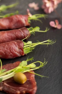 Slices of smoked salted meat with green pea microgreen on black concrete background. Side view,