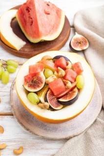 Vegetarian fruit salad of watermelon, grapes, figs, pear, orange, cashew on white wooden background
