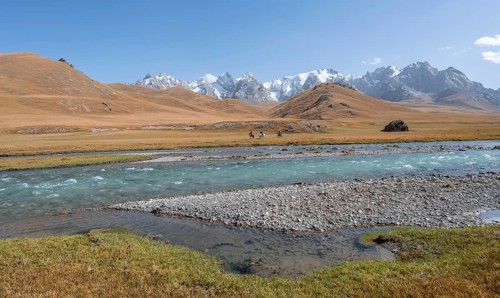 Riders on horses on the river bank, mountain landscape with yellow meadows and river Kol Suu,