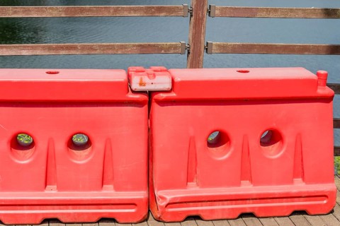 Two red plastic traffic barriers in front of fence on riverside boardwalk