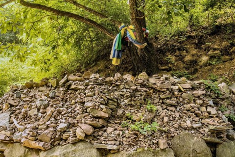 Colorful clothes wrapped around a tree beside numerous pebble stacks and loose stones in South