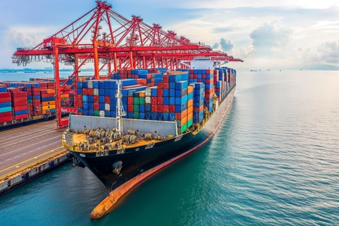 A large container ship in the harbour loaded with colourful containers under a partly cloudy sky,
