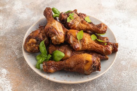 Smoked chicken legs with herbs and spices on a ceramic plate on a brown concrete background. Side