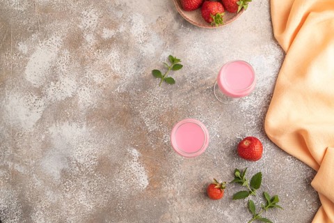 Sweet strawberry liqueur in glass on a gray concrete background and orange textile. top view, copy
