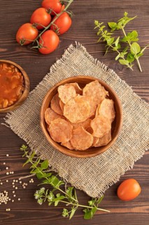 Slices of dehydrated salted meat chips with herbs and spices on brown wooden background and linen