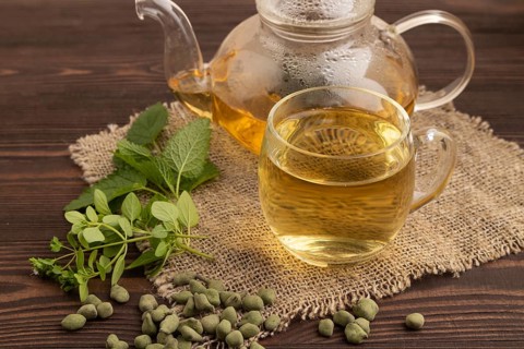 Green oolong tea with herbs in glass on brown wooden background and linen textile. Healthy drink