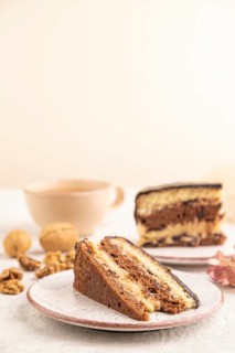 Chocolate biscuit cake with caramel cream and walnuts, cup of coffee on gray concrete background.