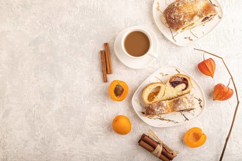 Homemade sweet bun with apricot jam and cup of coffee on gray concrete background. top view, flat