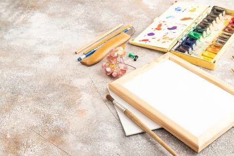 Drawing accessories set: brushes, pencils, watercolor, frame on brown concrete background. Side