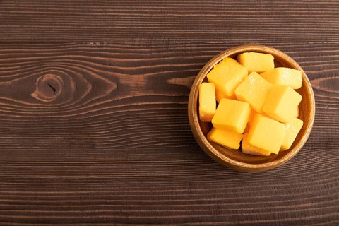 Dried and candied mango cubes in wooden bowls on brown wooden textured background. Top view, flat